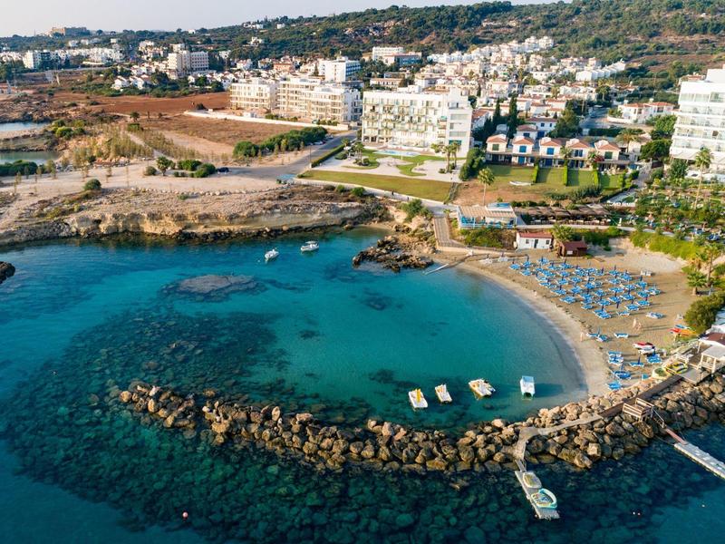 Baie côtière avec eau claire, brise-lames en pierre et village en arrière-plan.