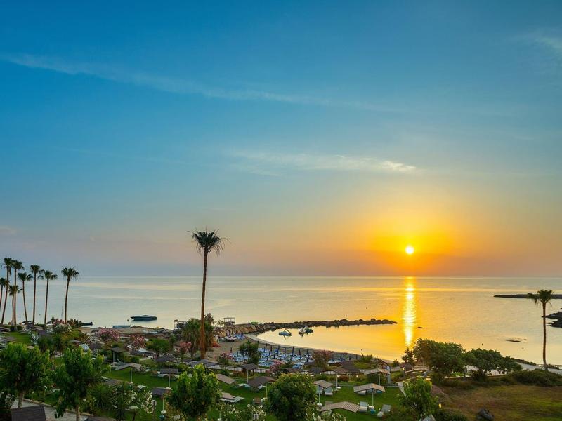 Coucher de soleil sur la mer avec des palmiers et une eau calme au bord.