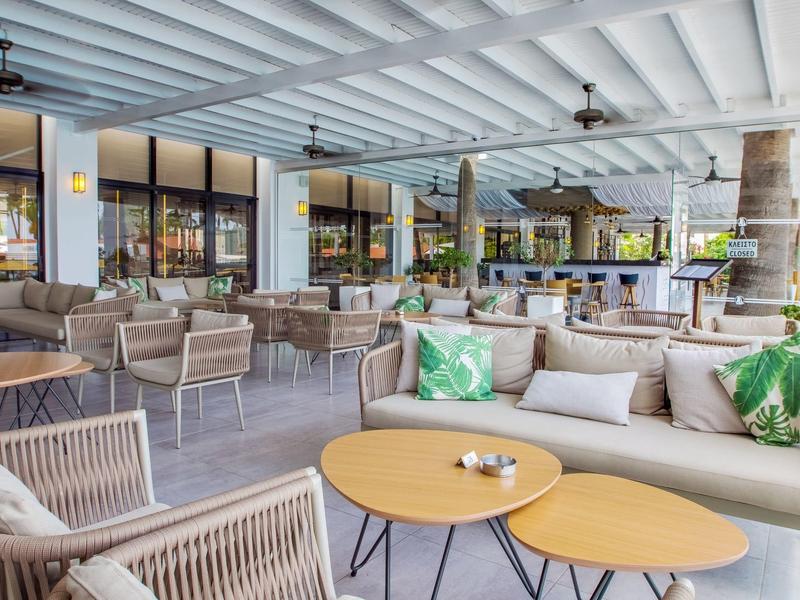 Espace lounge extérieur d'hôtel avec canapés, fauteuils, tables basses et décor vert.