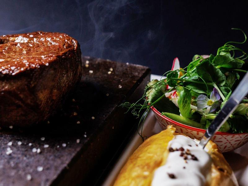Steak juteux avec salade verte fraîche et sauce blanche, sur planche en bois sombre.