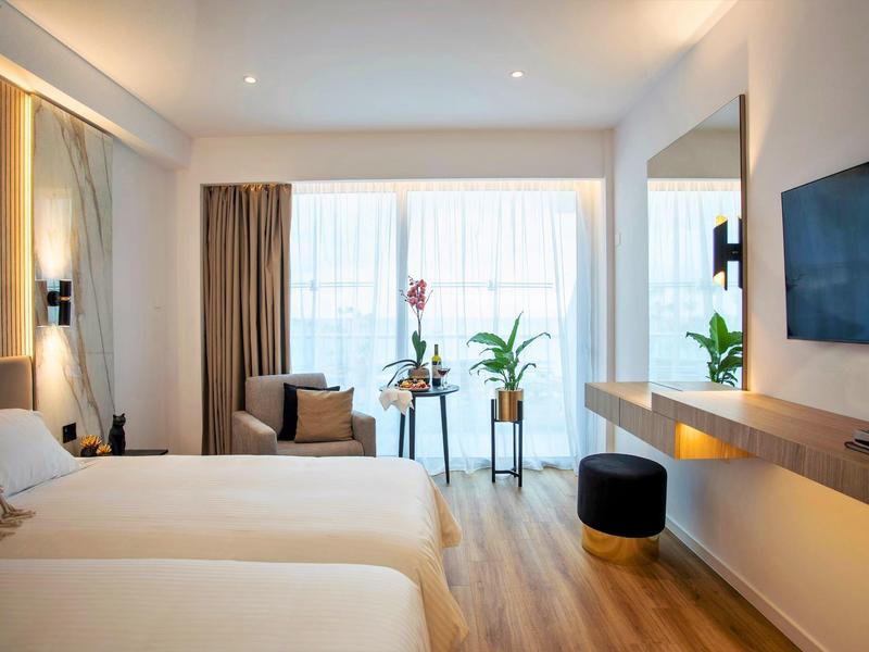 Chambre d'hôtel moderne avec deux lits simples, coin salon et grande fenêtre.