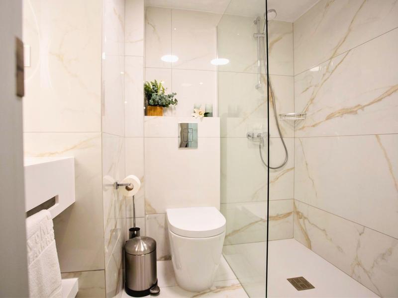 Salle de bain moderne et lumineuse avec douche, toilettes et carrelage en marbre blanc.