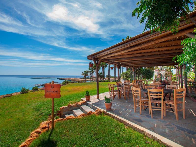 Restaurant en plein air avec chaises et tables en bois surplombant la mer sous un ciel bleu.