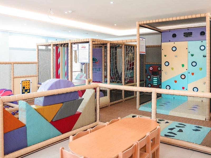 Mur d'escalade coloré et espace de sièges dans une salle de jeux intérieure lumineuse.