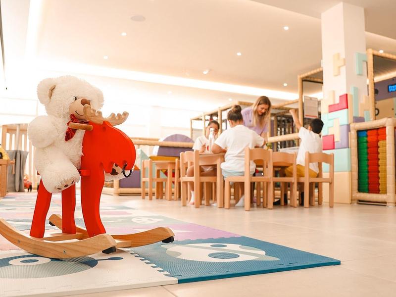 Espace de jeu clair pour enfants avec cheval à bascule et sièges dans un hôtel.