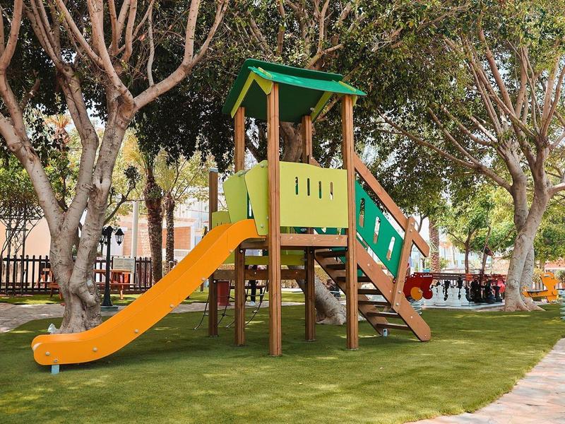 Aire de jeux avec toboggan orange dans un parc ombragé par des arbres.