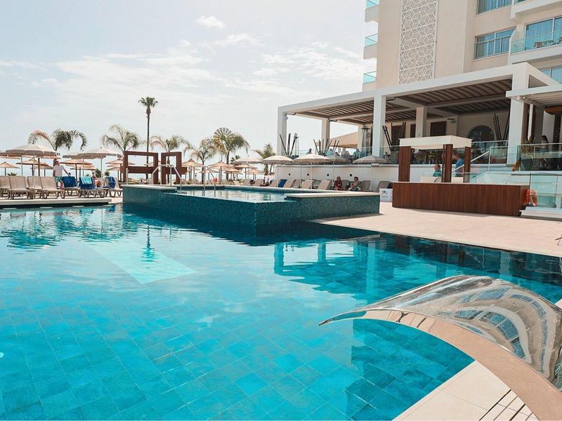 Piscine d'hôtel moderne avec eau claire, parasols et chaises longues, entourée d'un immeuble.