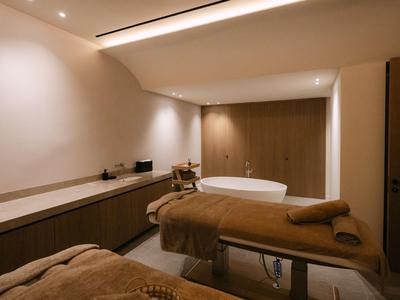 Gemütlicher Behandlungsraum mit Massagebank und Badewanne in warm beleuchtetem Hotel-Spa.