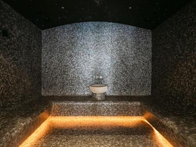Dunkler Spa-Ruheraum mit beleuchtetem Sitzpodest und zentralem Wasserbecken.