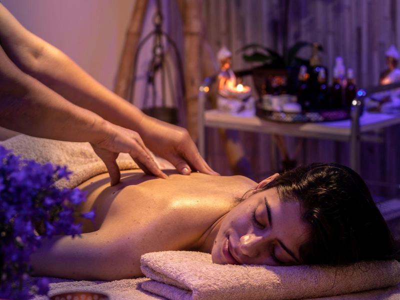 Eine Frau entspannt sich während einer Massage in einem gedämpften, lila beleuchteten Raum.