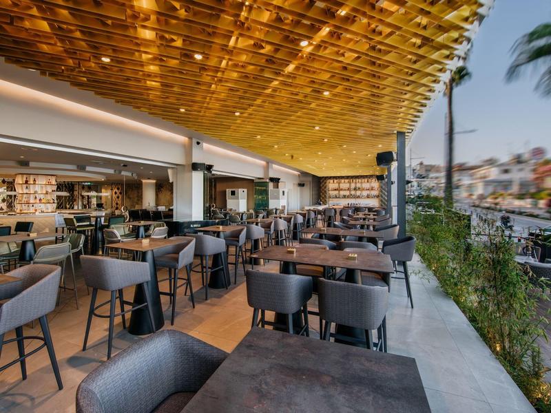 Moderner Außenbereich eines Restaurants mit Holzdach, grauen Stühlen und Blick auf die Stadt.