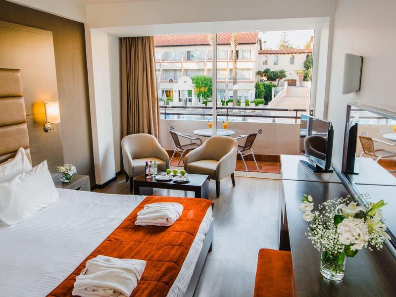 Modernes Hotelzimmer mit Doppelbett, Sitzbereich, Balkon und Blick auf Nachbargebäude.