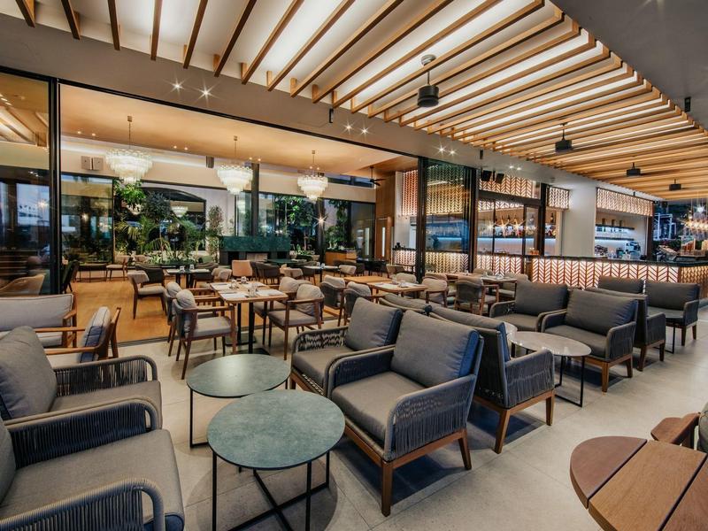 Modernes Restaurant mit Holzdecke, gemütlichen Sesseln und großen Glasfenstern.