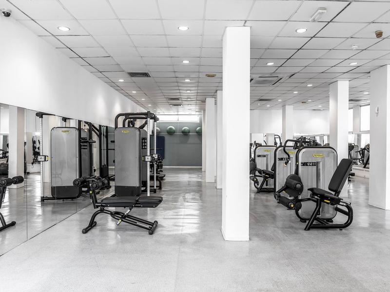 Großer heller Fitnessraum mit modernen Kraftgeräten und Spiegelwänden.