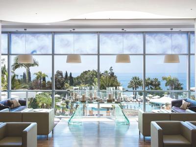 Modern lounge area with sofas in front of large windows overlooking pool and sea.