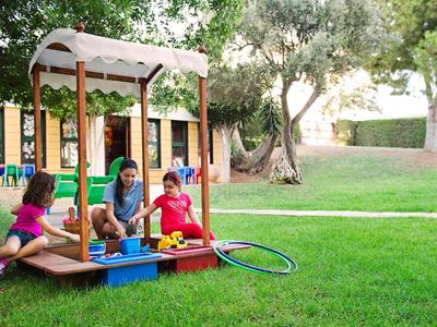 Children playing in a garden on a wooden playhouse with slide on a sunny day.