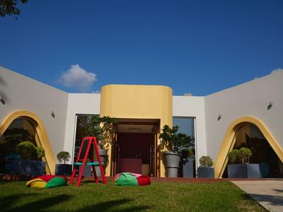 Modernes Gebäude mit weißen Wänden, gelben Bögen und Garten mit Spielgeräten bei klarem Himmel.