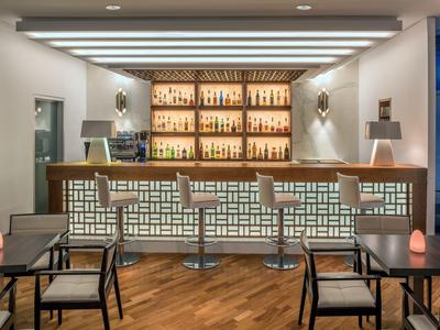 Moderner Hotelbarbereich mit stilvollen Hockern, beleuchtetem Tresen und Holzfußboden.