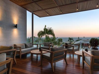 Offene Lounge mit Holzboden und bequemen Sesseln mit Blick auf Meer und Palmen bei Sonnenuntergang.