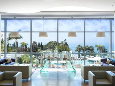 Modernes Lounge-Bereich mit großen Fenstern und Blick auf einen Pool und Palmen.