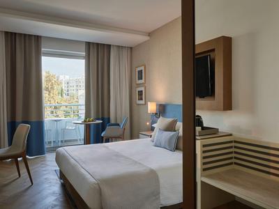 Modernes Hotelzimmer mit Doppelbett, Sitzbereich vor großem Fenster und Fernseher an der Wand.