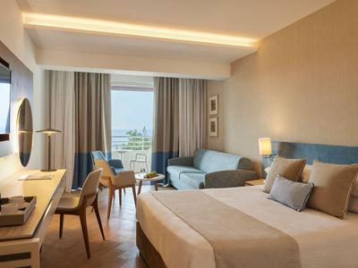 Modernes Hotelzimmer mit Doppelbett, Sofa, Schreibtisch und Meerblick vom Balkon.