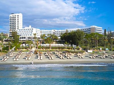 Modern hotel at a beach with sun loungers and umbrellas, surrounded by palm trees.