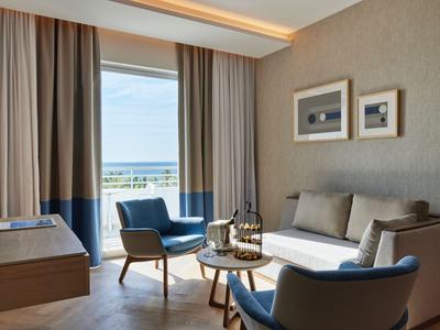 Modern eingerichtetes Wohnzimmer mit Sesseln, Sofa und großem Fenster mit Meerblick.