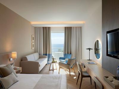 Modern eingerichtetes Hotelzimmer mit Meerblick, Bett, Sofa, Schreibtisch und Balkon.