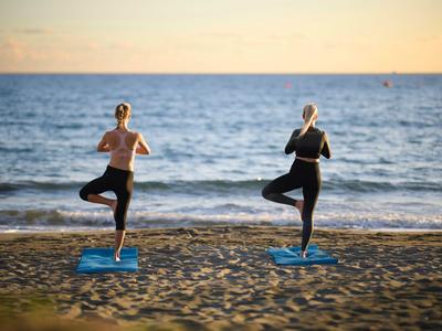 Zwei Personen praktizieren Yoga am Strand bei Sonnenuntergang, Blick auf das Meer.