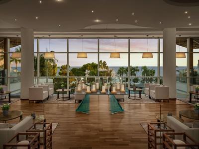 Modernes Lounge-Bereich mit Holzboden, weißen Stühlen und großen Fenstern, Blick auf Außenbereich und Natur.