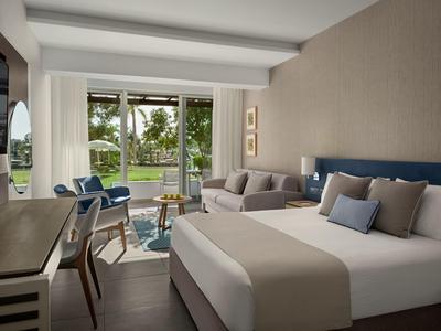 Modern eingerichtetes Hotelzimmer mit großem Bett, Sitzecke und Blick auf den Garten.
