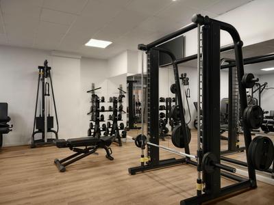 Moderner Fitnessraum mit Kraftgeräten, Hanteln und Hantelbank in hellen Räumen.