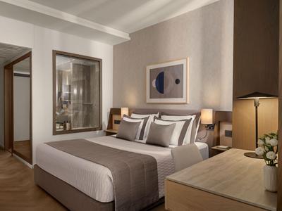 Modern eingerichtetes Hotelzimmer mit großem Bett, Nachttischen und Schreibtisch mit Lampe.