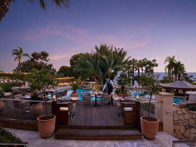 Abendliche Poollandschaft eines Hotels mit Palmen, Liegen und blau beleuchtetem Wasser.