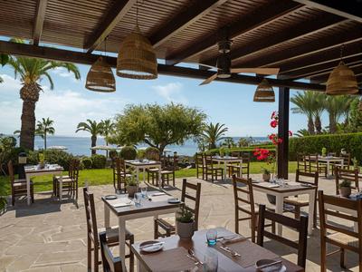 Offenes Restaurant mit Holzdach und Blick auf Garten mit Palmen und Meer im Hintergrund.