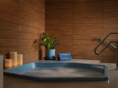 Ein ruhiger Whirlpool mit blauem Wasser, Holzwände und Kerzen für eine entspannende Atmosphäre.