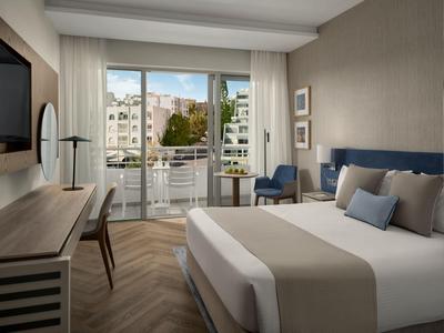 Modernes Hotelzimmer mit großem Bett, Stuhl, Schreibtisch und Balkon mit Stadtblick.
