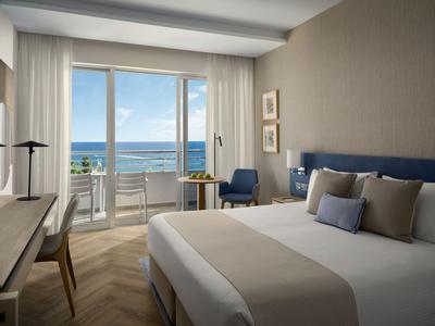 Modernes Hotelzimmer mit großem Bett, Sitzbereich und Meerblick durch große Fenster.
