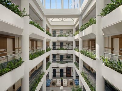 Modernes Hotelatrium mit weißen Wänden, Glasgeländern und Pflanzen in Kreuzform.