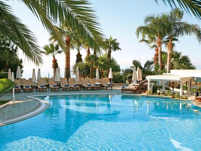 Inviting hotel pool with sun loungers and palm trees under a clear sky.