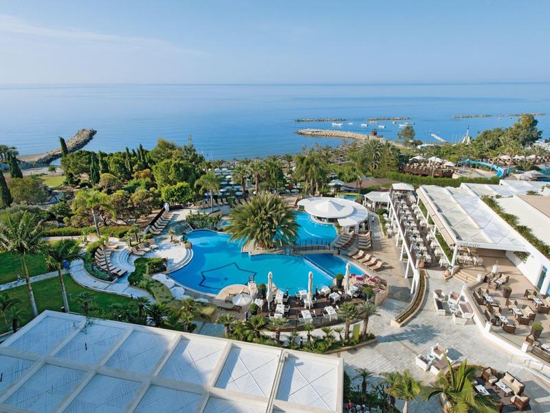 View of a hotel pool with sun loungers and sea view on a sunny day.