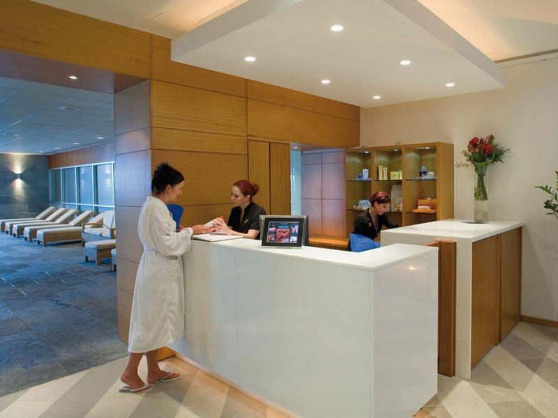 Hotel reception with two staff and a guest near a pool area.
