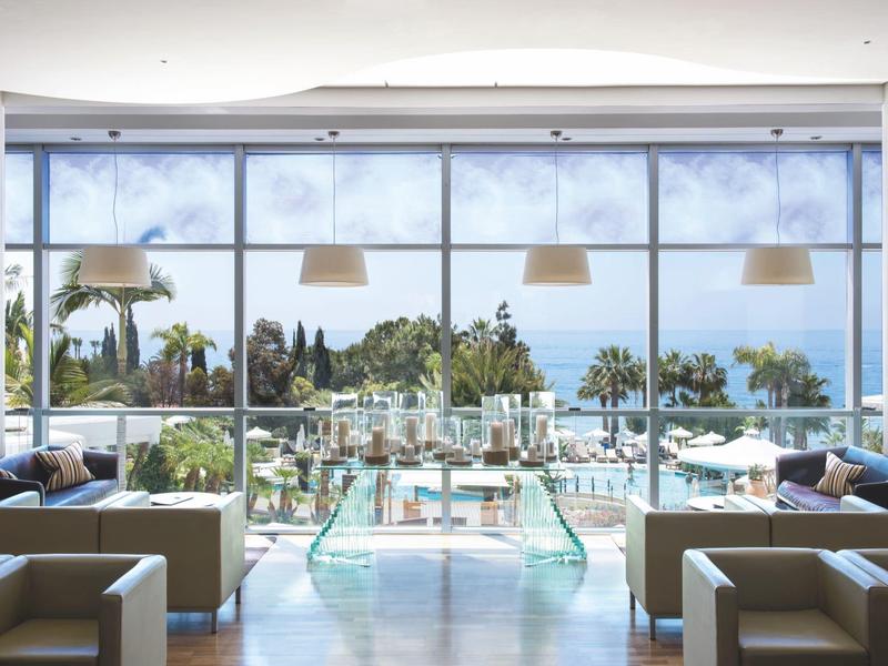 Modern lounge area with sofas in front of large windows overlooking pool and sea.