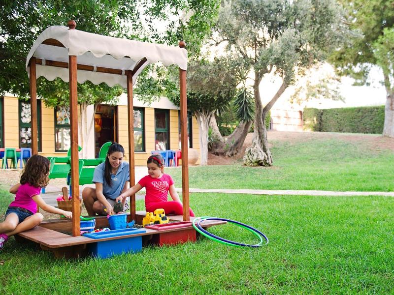 Children playing in a garden on a wooden playhouse with slide on a sunny day.