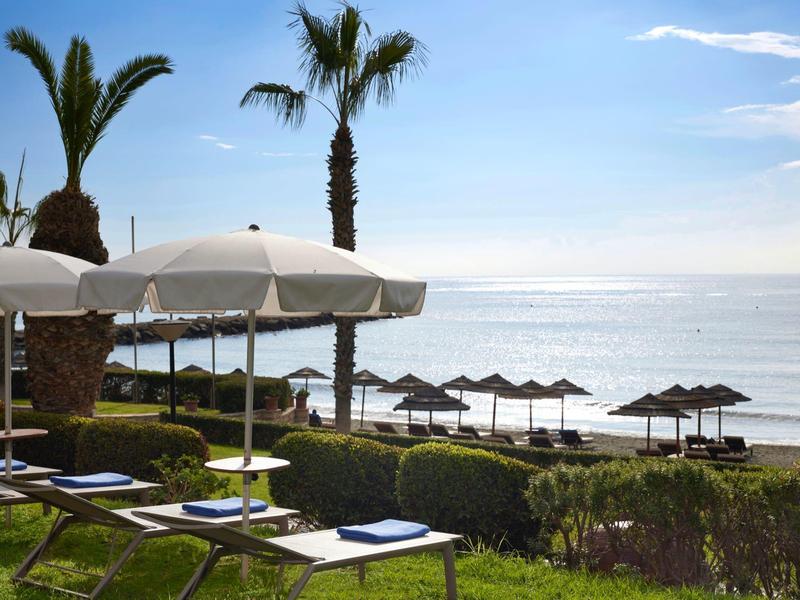 Sun umbrellas and loungers on a coast with palm trees and sea in the background.