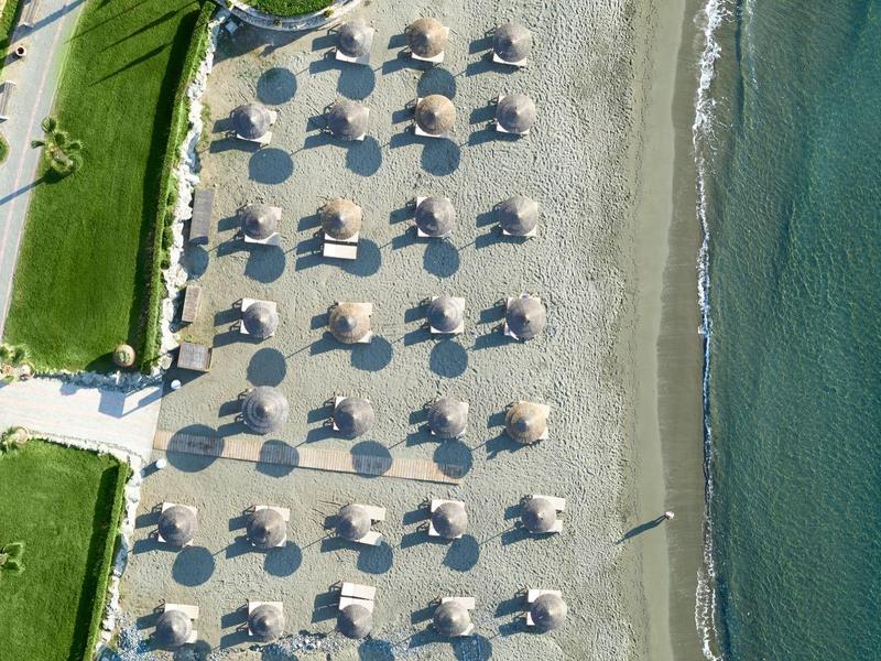 Aerial view of a beach with sun umbrellas, sand, adjacent sea, and green areas.