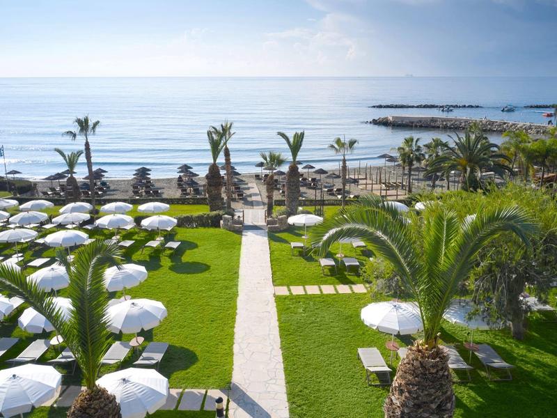 View of a hotel garden with sun loungers and umbrellas near the sea.