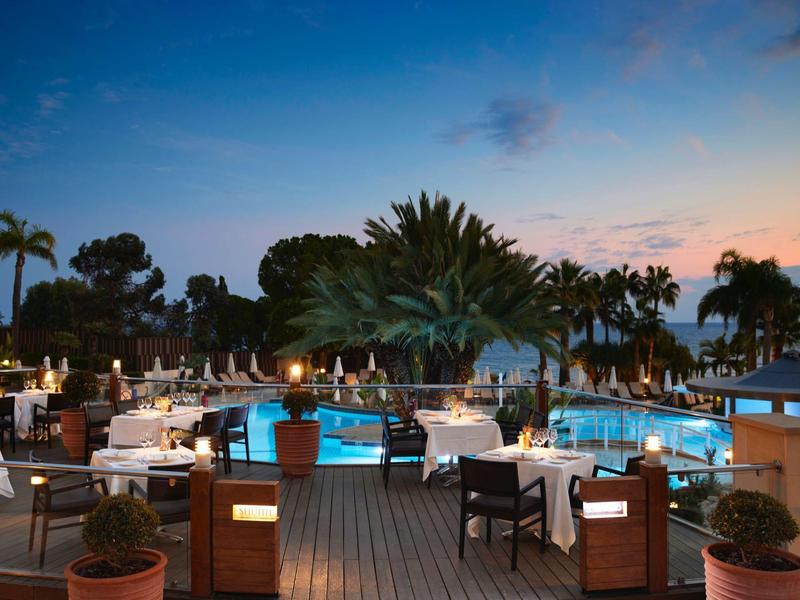 Luxury hotel outdoor area with pool and set tables at sunset.