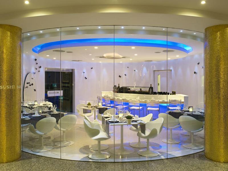 Modern hotel restaurant area with white chairs and blue-lit buffet.